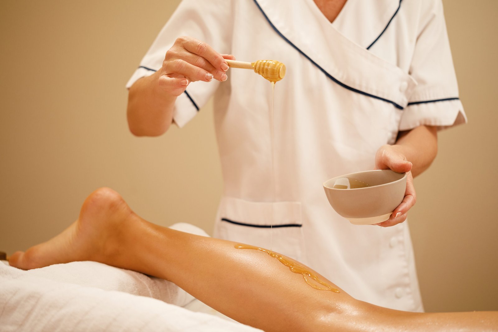 Unrecognizable therapist pouring honey while massaging woman's leg at spa salon.